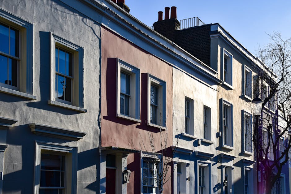 The image depicts a two-storey brick residential building with a pitched roof covered in light grey tiles. The facade features white-framed sash windows, with two visible on the upper floor and one pa